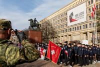 Na prawo i po lewo są salutujący żołnierze, lecz ci po prawej mają też w dłoni broń. Pomiędzy nimi pomnik